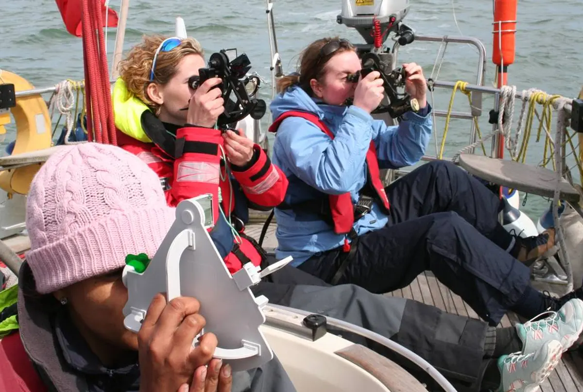 Participants practising celestial navigation with a sextant on a yacht