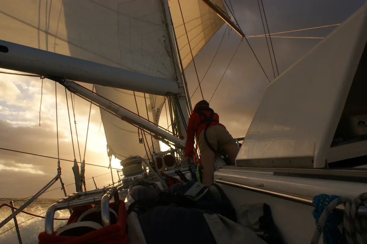 Crew on deck trimming sails on Atlantic passage under a setting sun